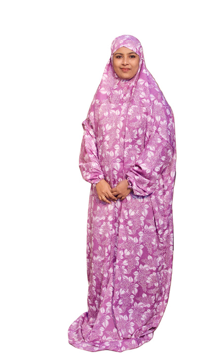 Woman wearing a pink floral abaya standing indoors with plants in the background